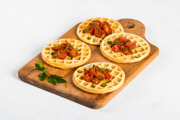 Mini waffles pizzas with baked tomatoes and parsley on a wooden board on a light background