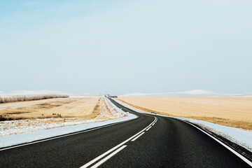 Winter clear road in Khakassia with fields and mountains in the background