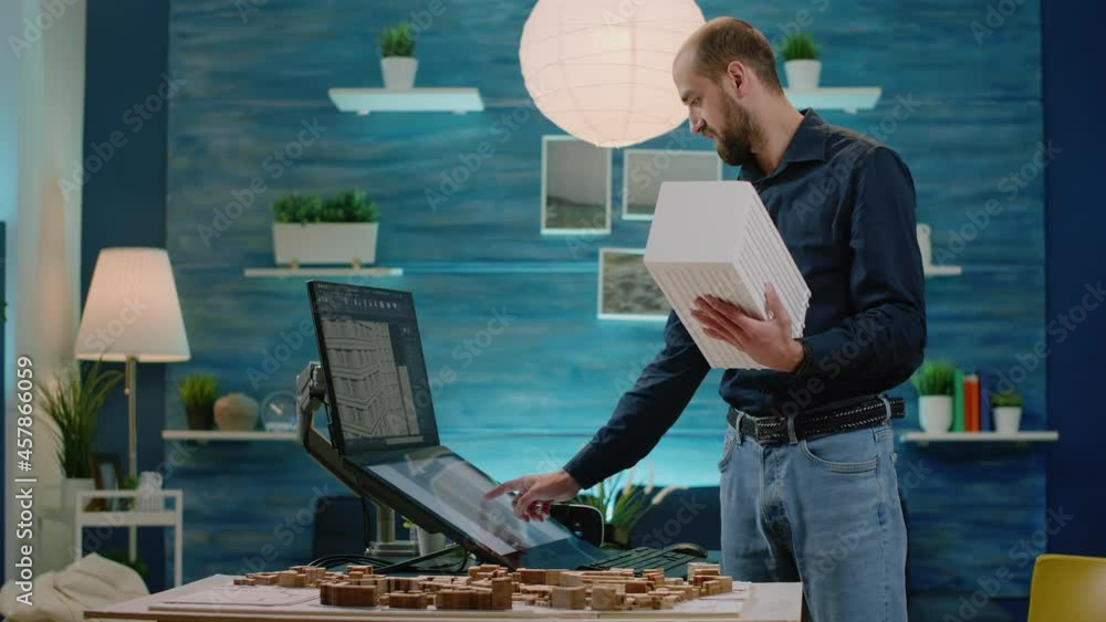 Poster man working as architect holding maquette and using touch screen monitor for building model project.