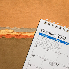 October 2021 - spiral desktop calendar against abstract paper landscape in earth tones, time and business concept