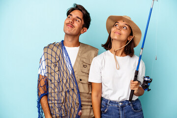 Young mixed race fisher couple isolated on blue background dreaming of achieving goals and purposes
