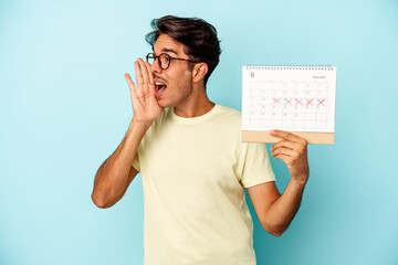 Young mixed race man holding calendar isolated on blue background shouting and holding palm near...