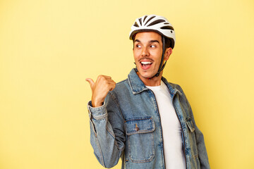 Young mixed race man wearing a helmet bike isolated on yellow background points with thumb finger away, laughing and carefree.