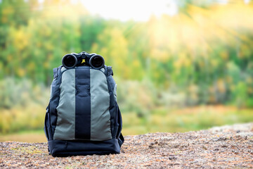 Matching backpack with binoculars on the high bank of the river. Equipment for the campaign.