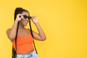 Trendy glasses. Eyewear banner. Optics fashion. African happy smiling woman in stylish sunglasses isolated on yellow empty space background.