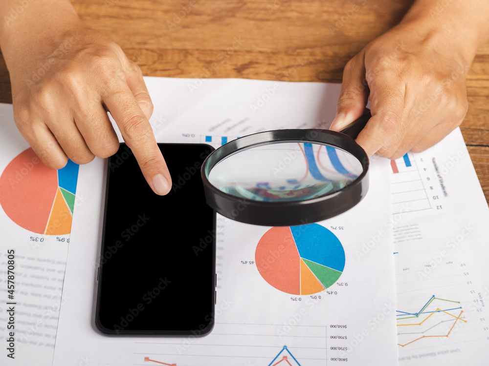Aufkleber hand of holding a magnifying glass reading financial data report and using a smartphone while sittin