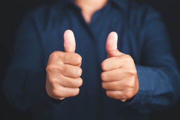 Midsection of businessman showing thumbs up while standing with a black background in the studio. Close-up photo. Finger gesture OK
