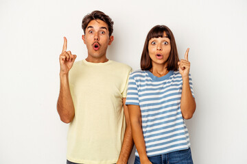 Young mixed race couple isolated on white background pointing upside with opened mouth.