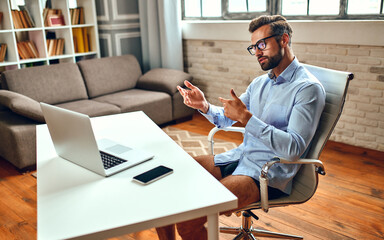 A man in a shirt and shorts sits at a table and talks on a video call, an online business...