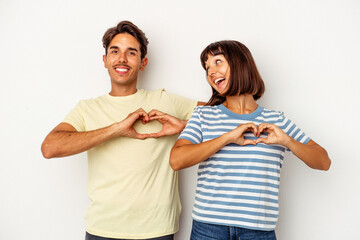 Young mixed race couple isolated on white background smiling and showing a heart shape with hands.