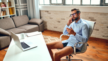 A man in a shirt and shorts sits at a table and talks on a video call, an online business...