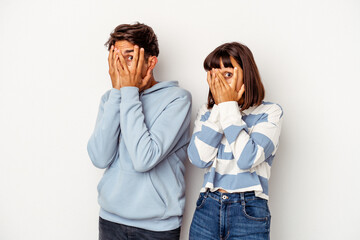 Young mixed race couple isolated on white background blink through fingers frightened and nervous.