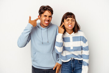 Young mixed race couple isolated on white background covering ears with hands.