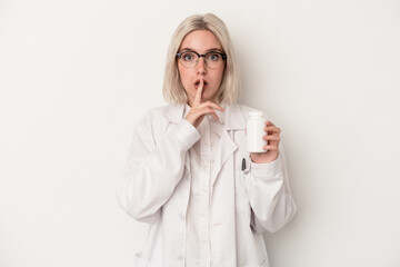 Young pharmacist woman holding pills isolated on white background keeping a secret or asking for...