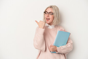 Young caucasian student woman holding books isolated on white background points with thumb finger...