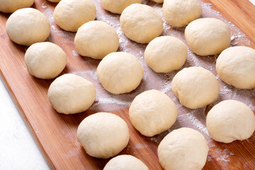 Fototapeta na wymiar Yeast dough balls on the wooden board with flour. Proofing to bake buns, bread or pizza 
