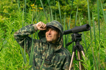 man birdwatcher makes field observation with a spotting scope among the thickets in a river valley