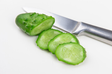 The cut cucumber with the knife on the white table