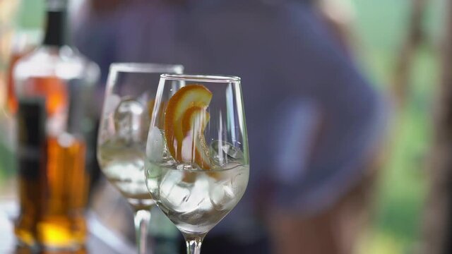 Bartender mixes alcoholic cocktails at bar with slice of orange and ice.