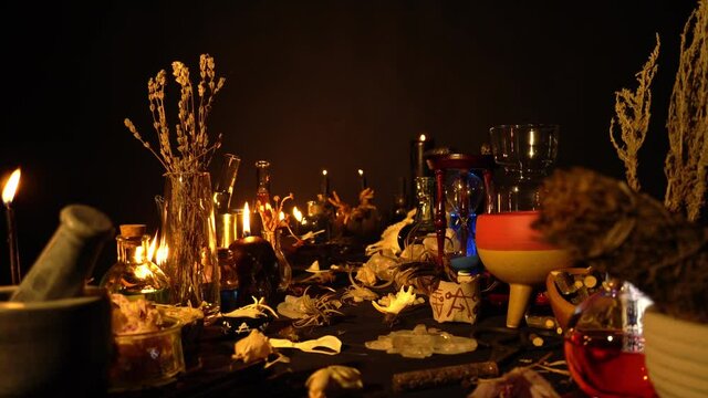 Occult and esoteric witch doctor still life. Halloween background with magic objects. Black candles, skull, crystal stones, and potions vials on witch table. Mystic witchery background with weeds.