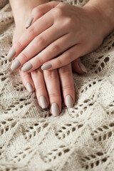Matt nude beige nails close up. Winter or autumn manicure, woman hand on warm sweater