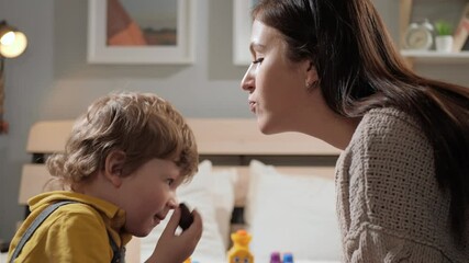 Mom kisses baby. Mother and child are playing in evening while sitting on bed and woman kisses her baby. Close-up and slow motion