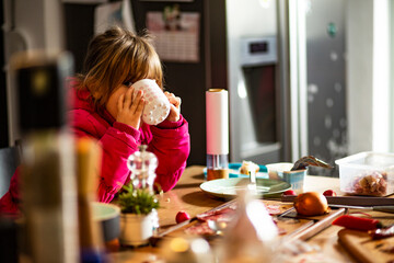 Cute little girl drinking tea, in a kitchen. 
Young Caucasian girl drinking milk, at home, in a kitchen.