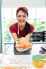 A beautiful woman in an apron holds bread and smiles while standing in a bakery.
