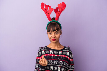Young mixed race woman with reindeer hat celebrating Christmas isolated on purple background  pointing with finger at you as if inviting come closer.