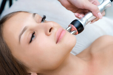 Young woman getting RF face lifting procedure in beauty salon.