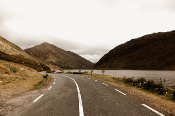 Fototapeta premium An empty rural road and a stunning landscape in Ireland. Mountains, hills and a lake next to the road. 