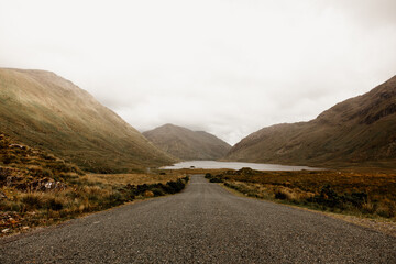 An empty rural road and a stunning landscape in Ireland. Mountains, hills and a lake at the end of the road. 