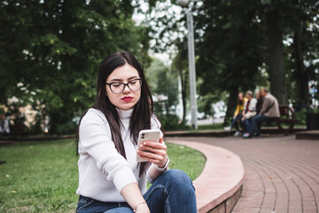Beautiful stylish girl in jeans and a white sweater outdoors in the park with a phone