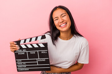 Young latin woman holding clapperboard isolated on pink background  laughing and having fun.