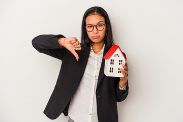 Young business latin woman holding a toy house isolated on white background  showing a dislike...