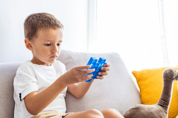 Soft stuffed toys with bubbles. Child plays with blue pop-it in form of puzzle. Cheerful boy holds in his hands a blue toy anti-stress pop it. 