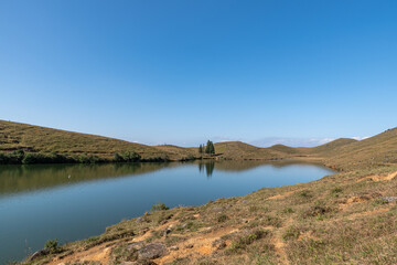 Under the blue sky, the natural lake on the meadow has yellow grass and blue water