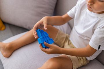 Boy smiling and playing with blue pop it fidget toy. Push bubble fidget sensory toy - washable and reusable stress relief toy. Antistress toy for child with special needs. Mental health concept