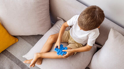 Little boy plays square rubber fidget toy Pop It. Blue-colored anti stress and tactile toy for all...
