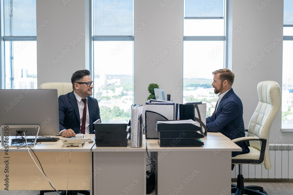 Poster two confident businessmen sitting in front of computer monitors while working in office