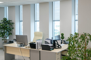 Pair of desks with computer monitors and documents standing along windows in large open space office