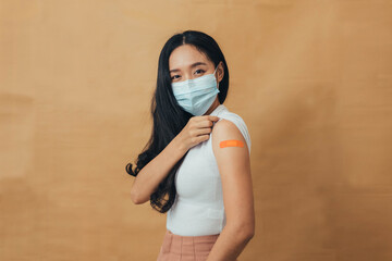 Asian woman showing shoulders after getting a vaccine. Happy woman showing arm with band-aids on...
