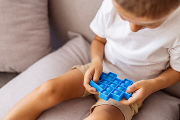 Little boy plays square rubber fidget toy Pop It. Blue-colored anti stress and tactile toy for all...