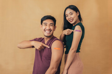 Asian man and woman showing shoulders after getting a vaccine. Happy couple showing arm with band-aids on after vaccine injection. - obrazy, fototapety, plakaty