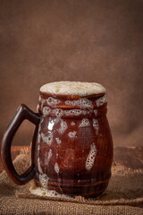 Beer clay brown mug with kvass on a wooden table on a dark background. A traditional drink made of...