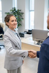 Obraz premium Young businesswoman in grey formalwear looking at colleague durng handshake
