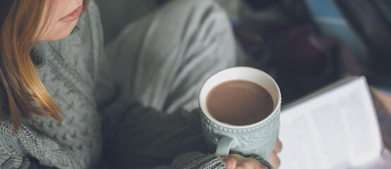 Winter still life concept. Young girl holding cacao mug, reading book. Season holiday, hygge concept