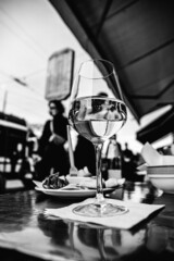 Close up shot from below of a glass of white wine on the table of a cocktail bar in the city. Happy hour or aperitif time in busy downtown Milan.
