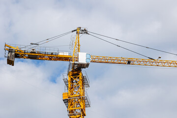 Yellow tower crane. Construction site with crane. Construction crane at blue sky background. Tower crane against blue sky with clouds. Tower crane working at construction site.