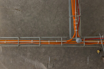 Cable tray with orange wires and metal duct show above t-bar grid below concrete of upper floor at construction site of building. Fire extinguishing and fire alarm system orange wires - obrazy, fototapety, plakaty